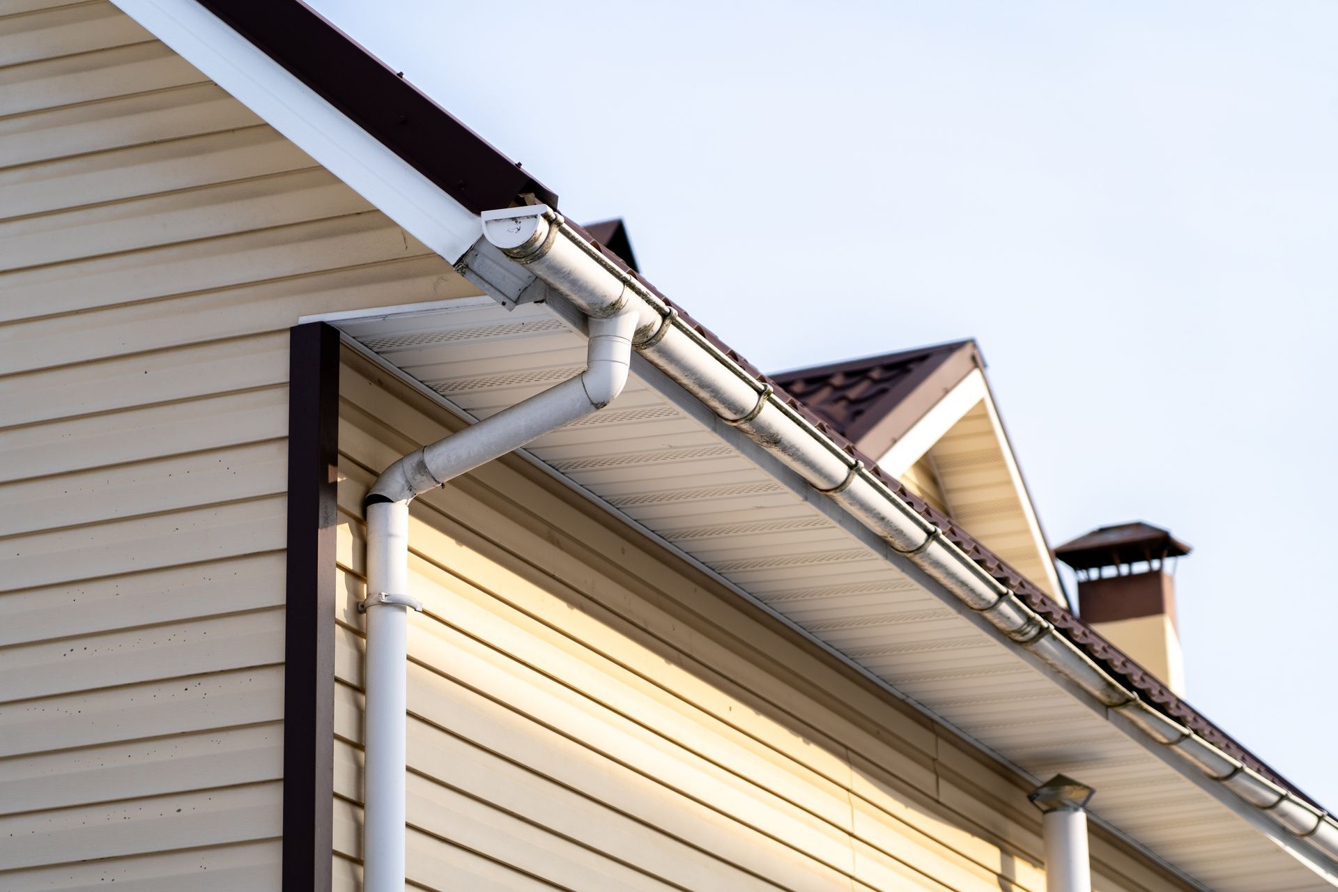 House roof gutter and downspout on beige siding under a clear sky