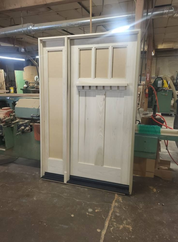 Wooden door with sidelight, unfinished, in a workshop setting.