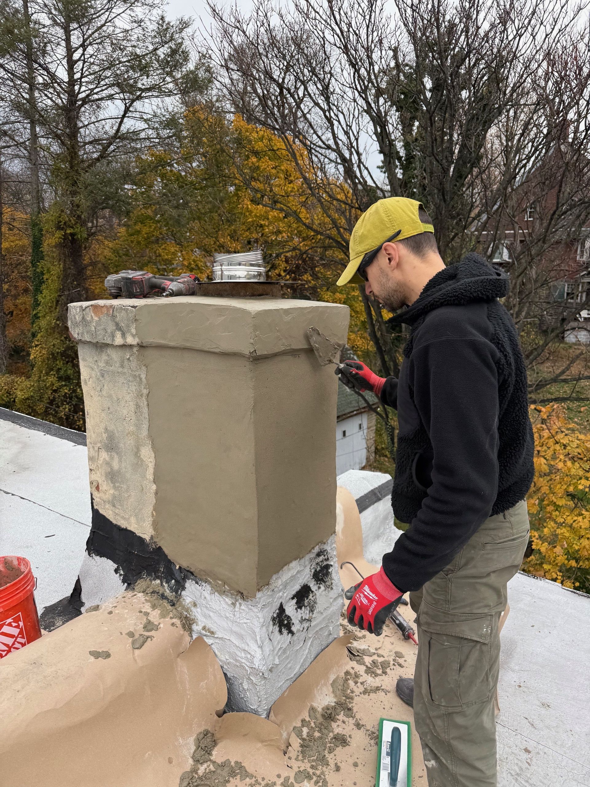 A man is standing on top of a roof fixing a chimney.