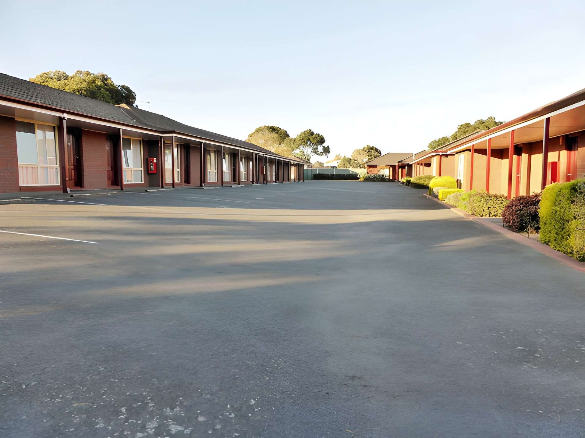 Motel parking lot with rows of single-story rooms and a wide asphalt drive at sunset