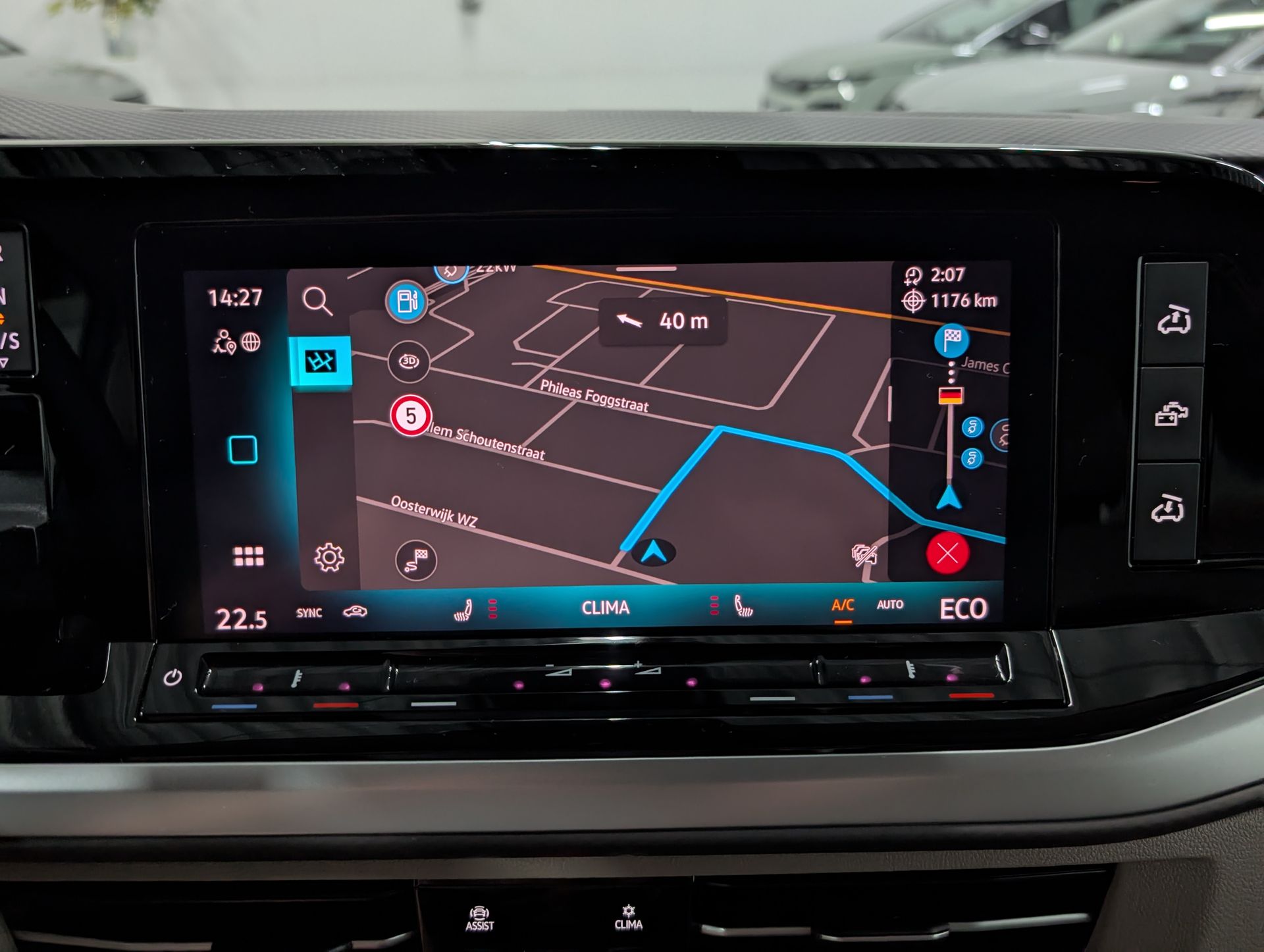 Op het dashboard van de auto wordt een navigatiekaart met een blauwe route weergegeven. Bedieningselementen voor klimaatregeling en andere instellingen. Dit is een Volkswagen California eHybrid 