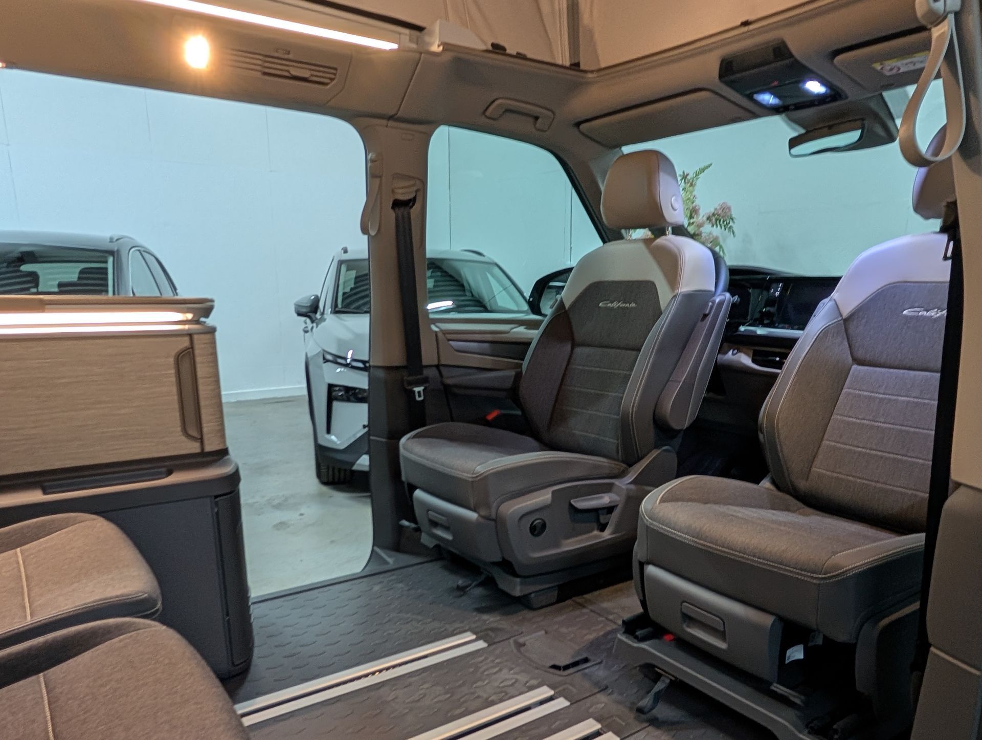 Interieur van een Volkswagen California eHybrid Campervan, met voorstoelen en opbergvakken. Grijze en beige tinten overheersen.
