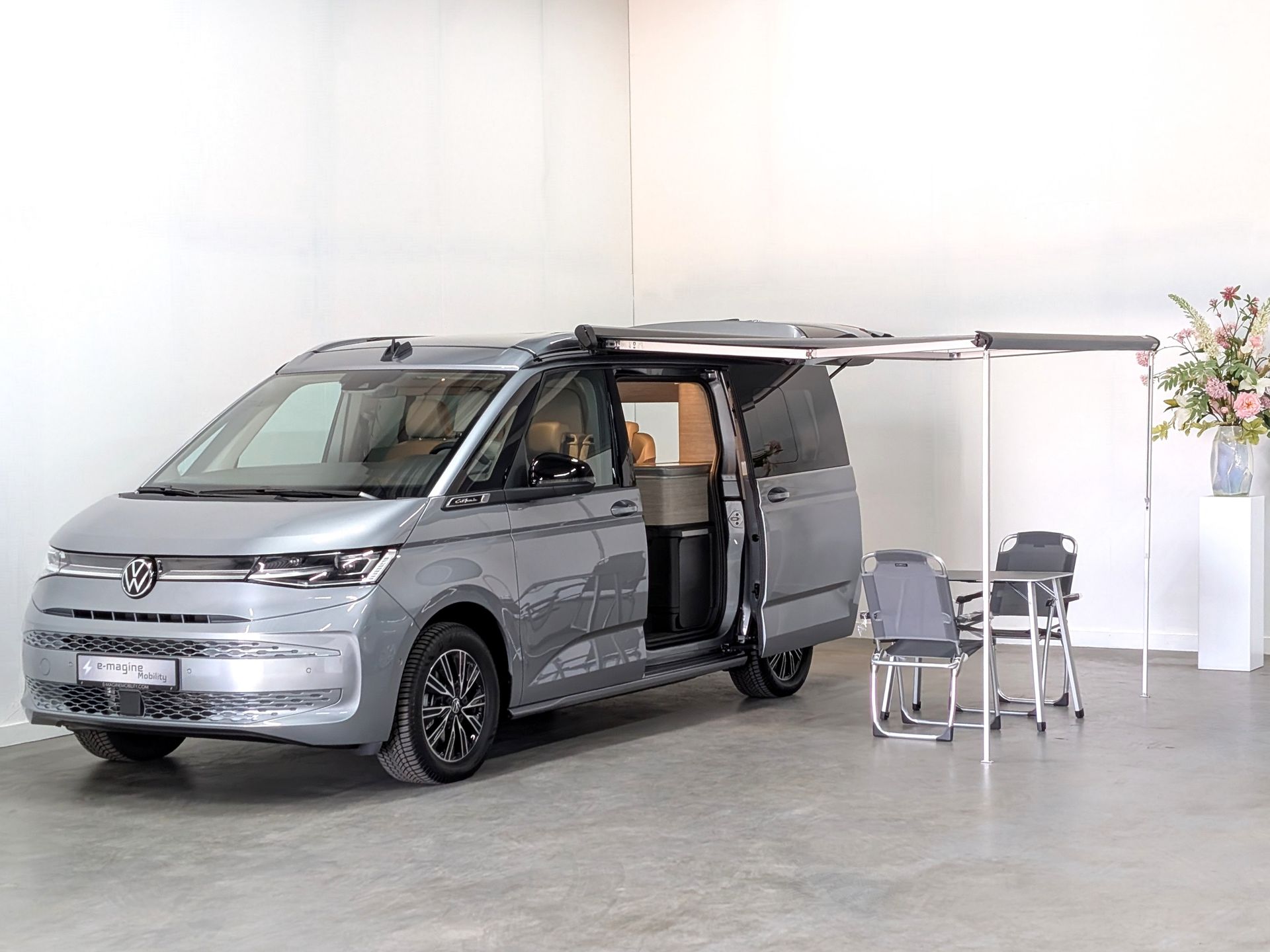 Volkswagen California Ocean eHybrid in de kleur Mono Silver met luifel uitgeklapt en een tafel en stoeltjes voor de camper