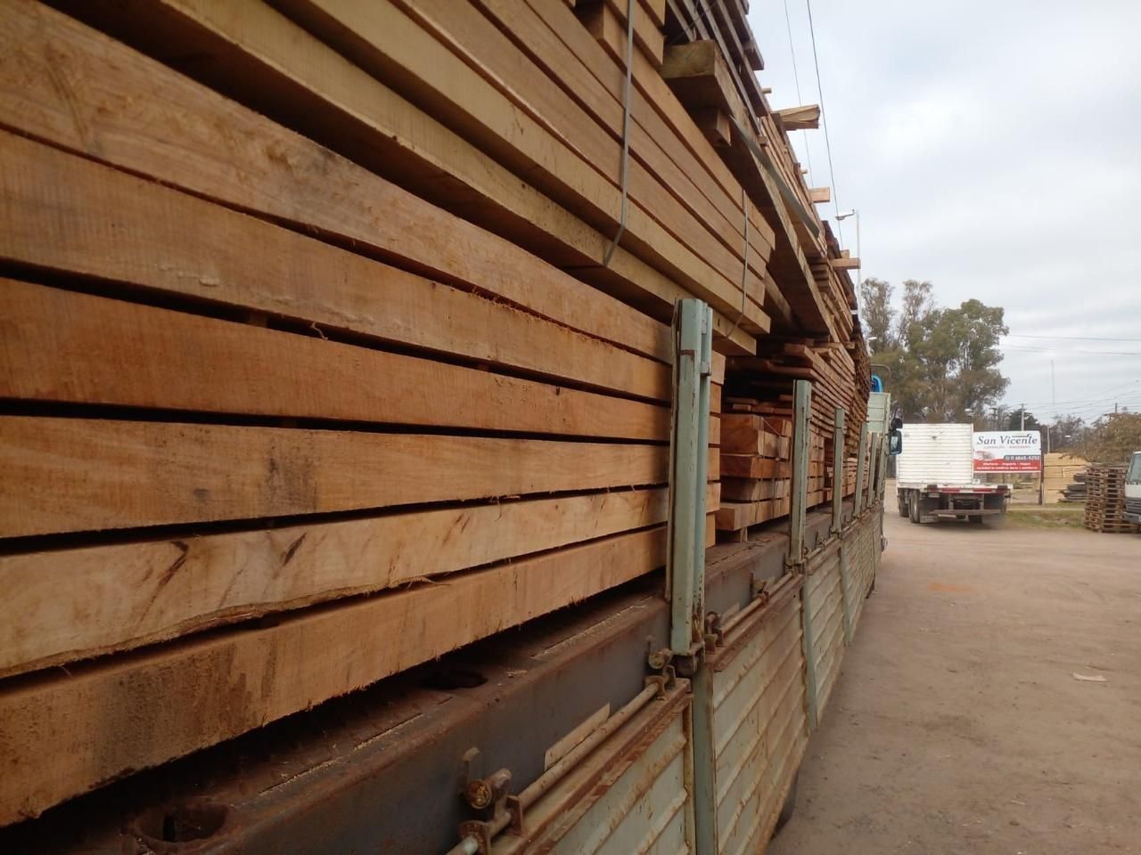 Camión o remolque con laterales de madera estacionado en un camino de tierra junto a una cerca y un terreno baldío.
