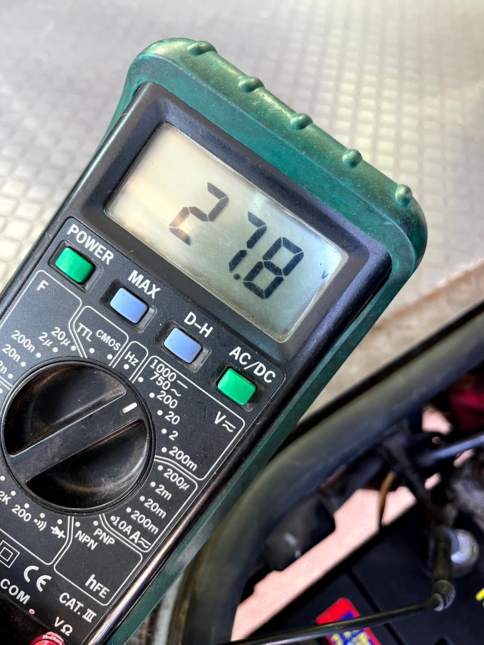 Multimeter showing a reading of 27.8, presumably measuring voltage. Green and black device.