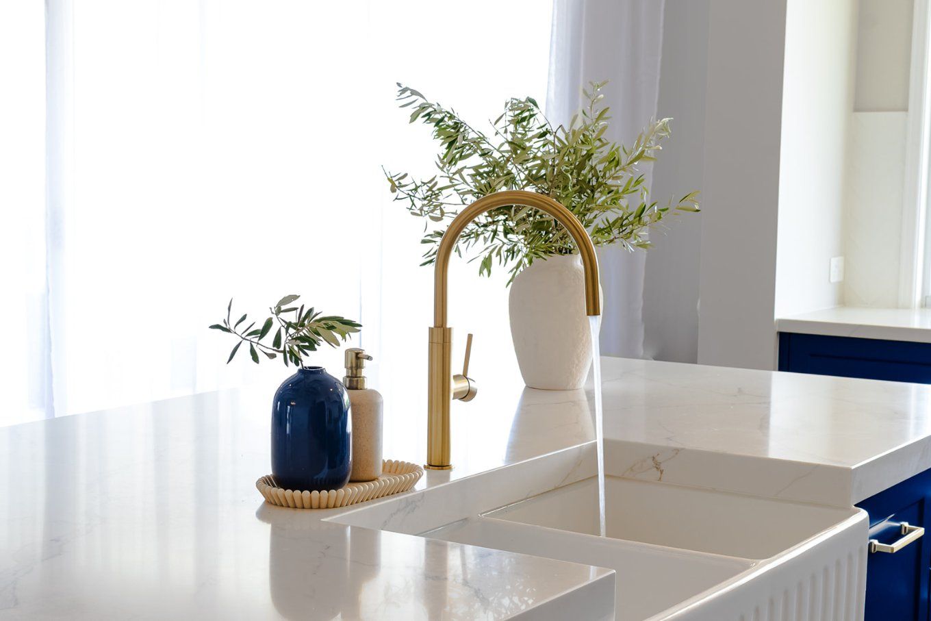 Gold Faucet With Running Water Over a White Sink on a Bright White Countertop — Truline Cabinets In Tuchekoi, QLD