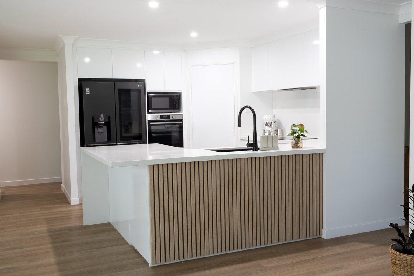 Modern White Kitchen With a Wooden Slatted Island and Black Appliances — Truline Cabinets In Tuchekoi, QLD