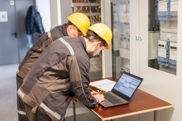 Two men in hard hats are looking at a laptop on a table.