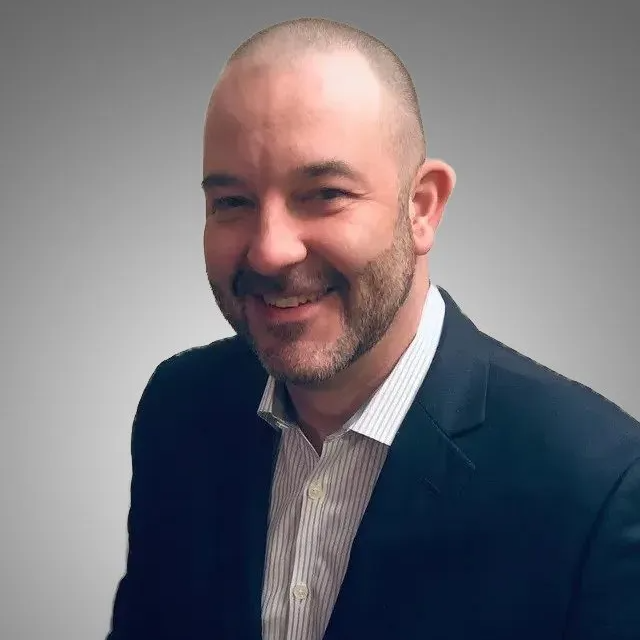 A man with a beard is wearing a suit and smiling.