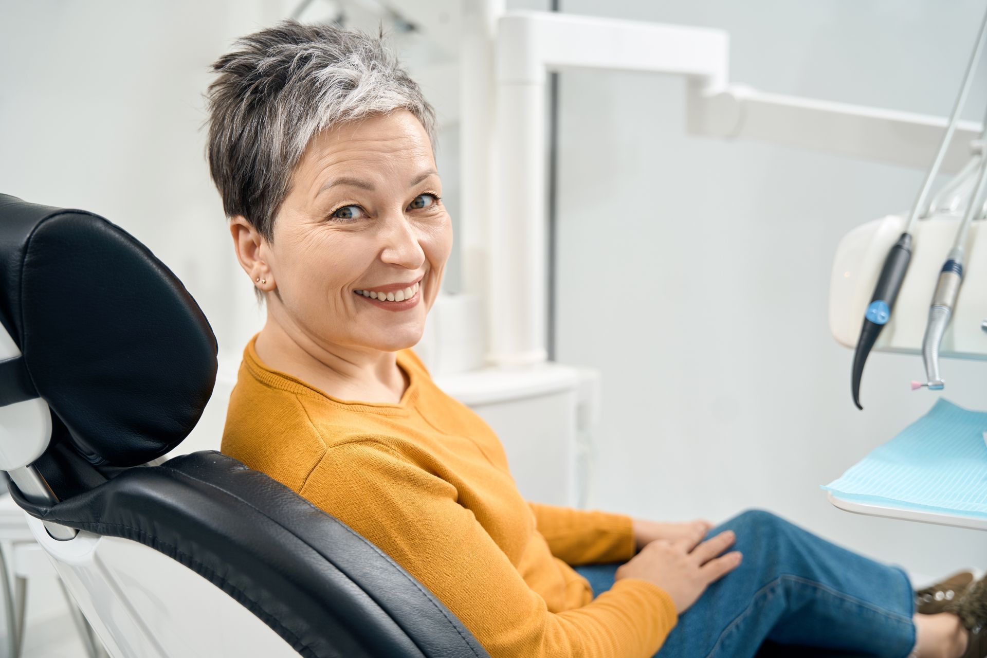 Woman sitting in dental chair. Woman smiling with dental equipment behind her.