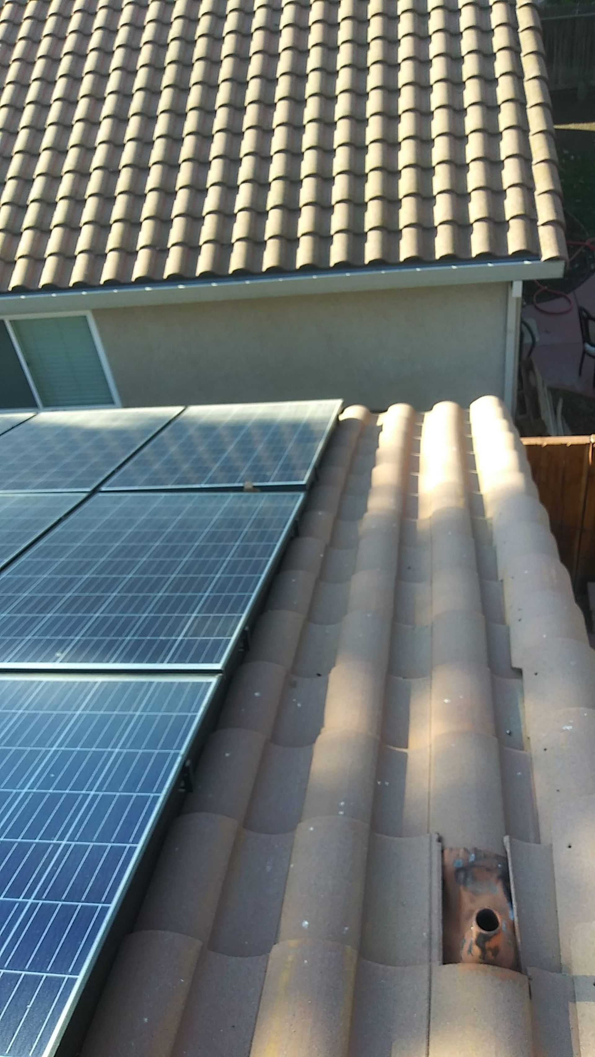 Solar panels installed on a brown tiled roof, with another tiled roof visible above.