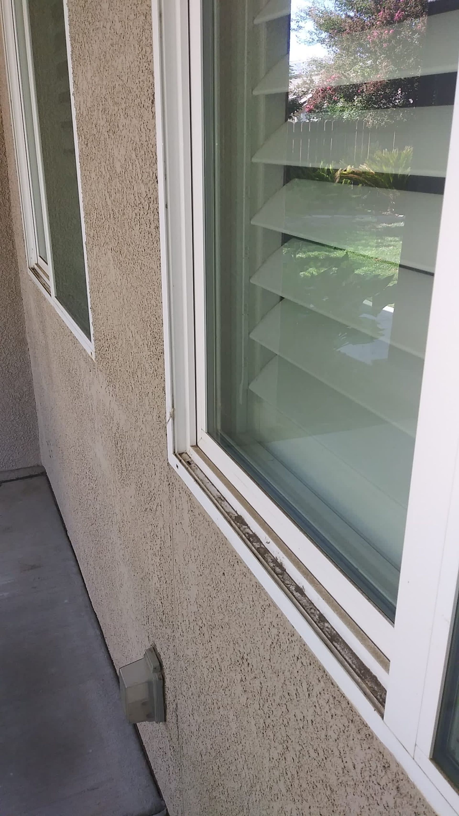 Window with white frame, set in beige textured wall, with closed window blinds.