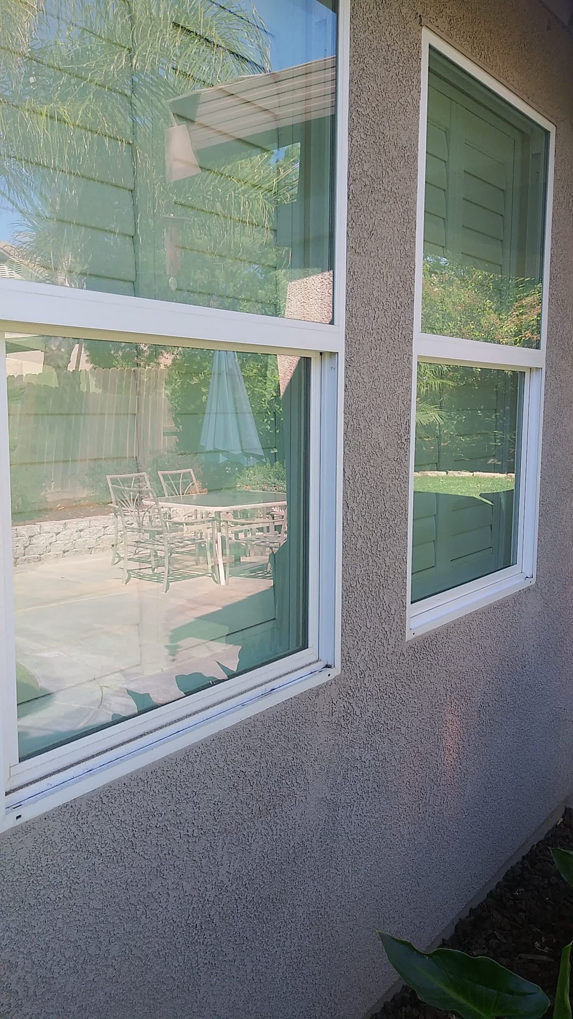 White framed windows on a textured beige wall, reflecting a patio with furniture and greenery.