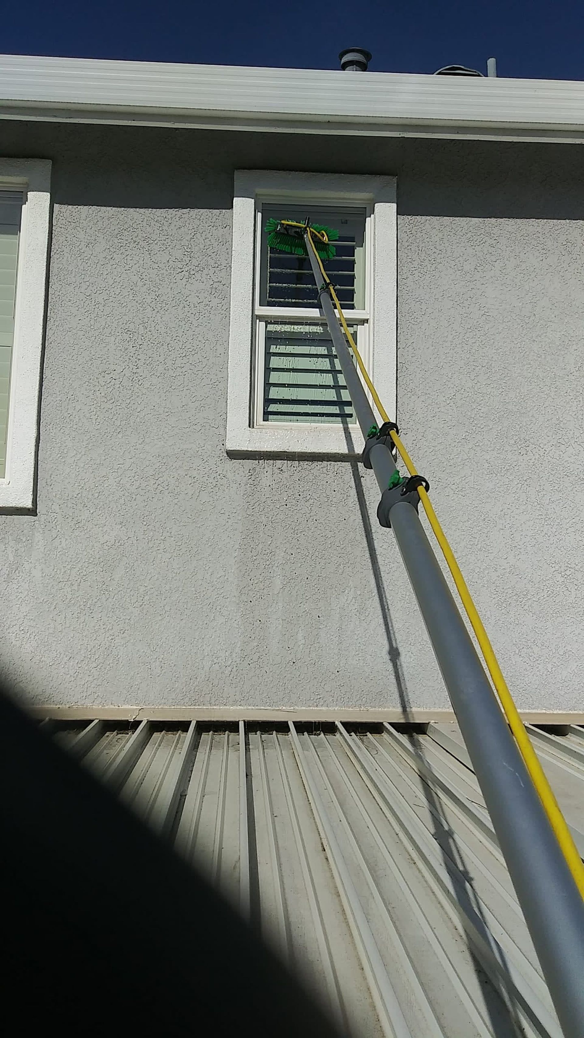 Window being cleaned with a long-handled tool on a stucco building.
