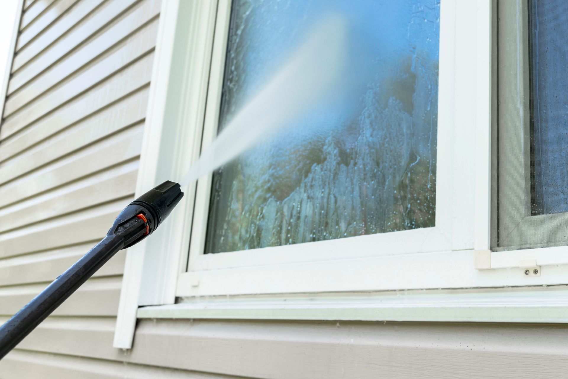 Pressure washing a house window with a spray wand