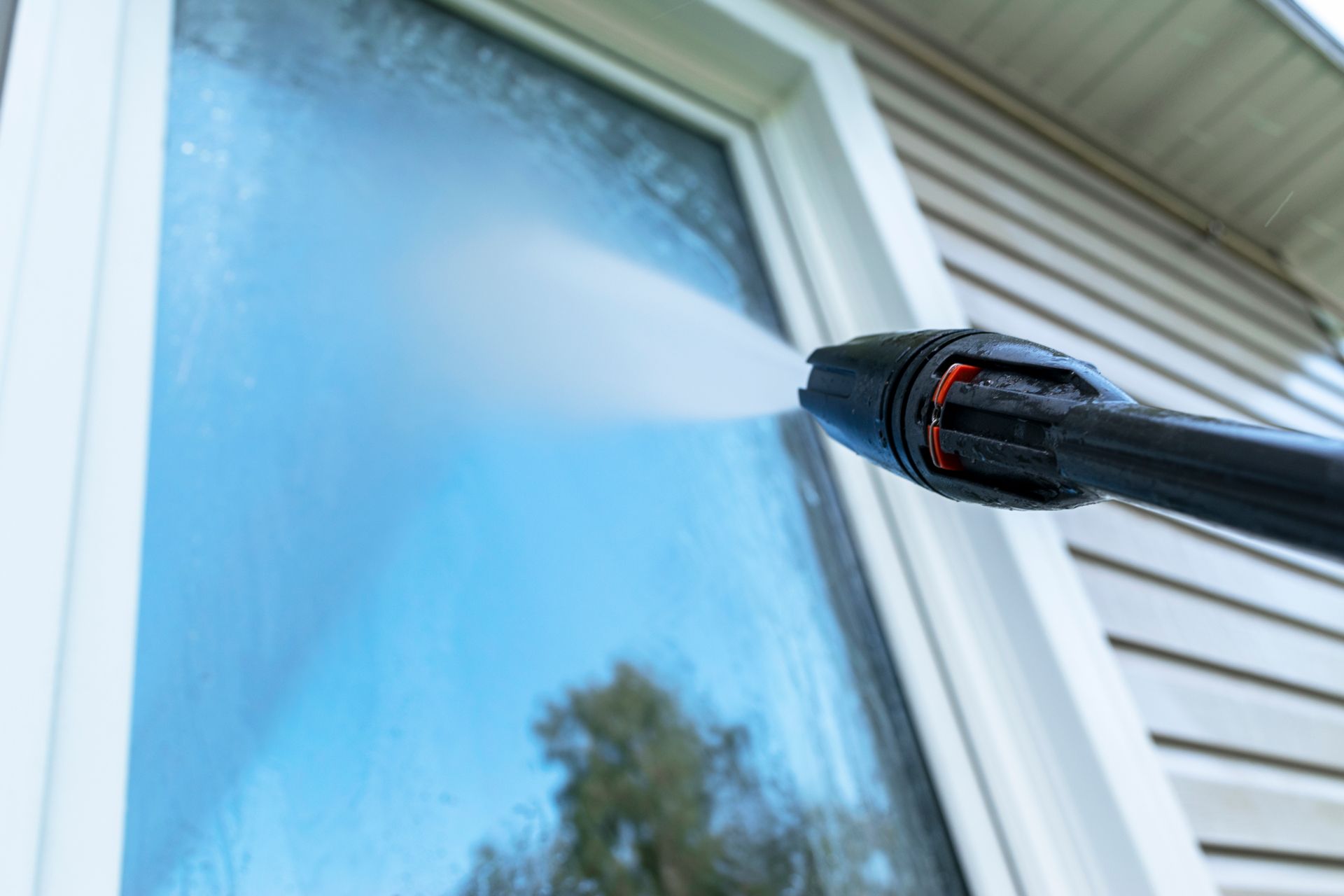 Pressure washer spraying a blue-tinted window on a house exterior
