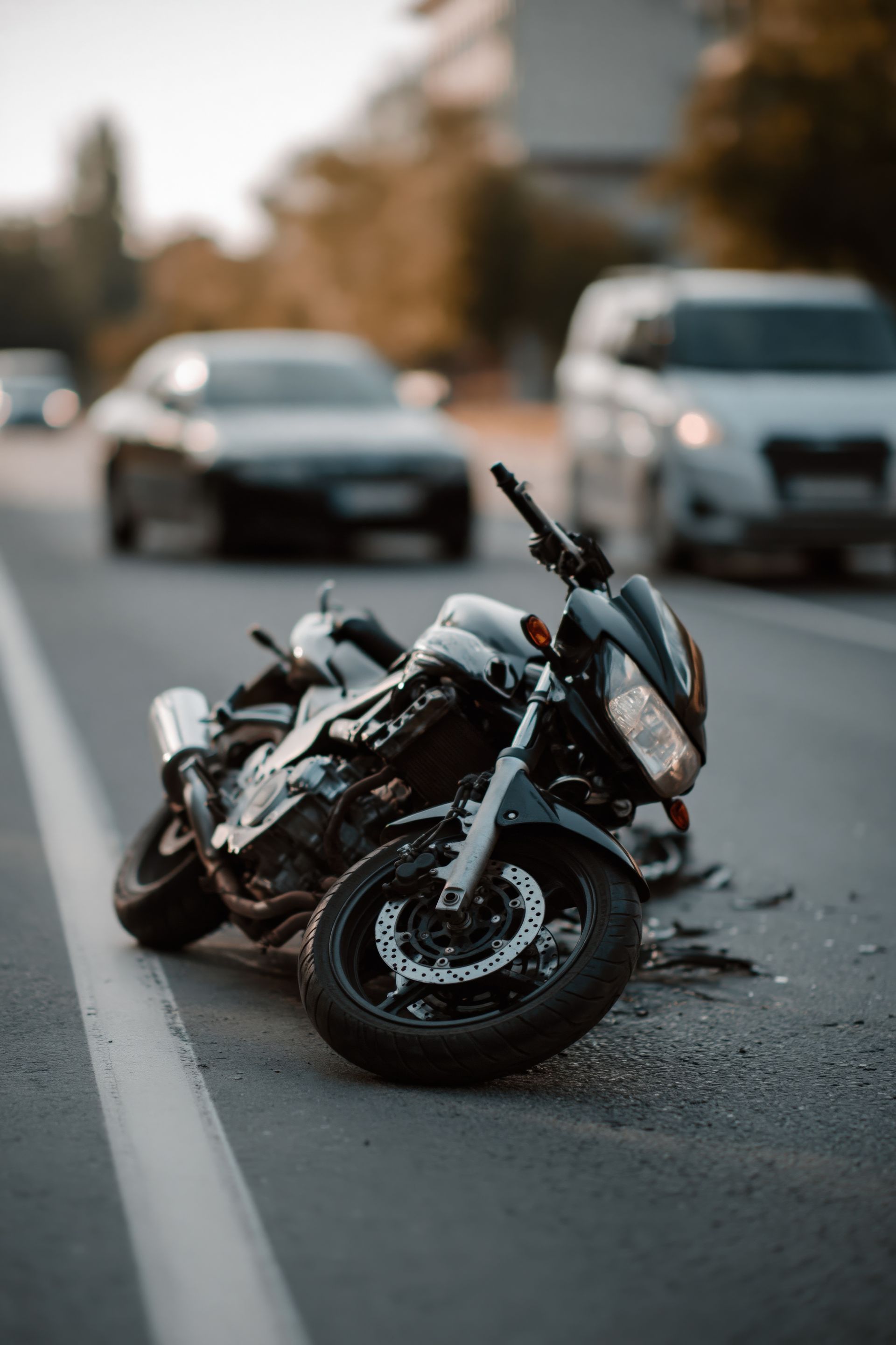 Damaged motorcycle lying on a road with two blurred cars behind it