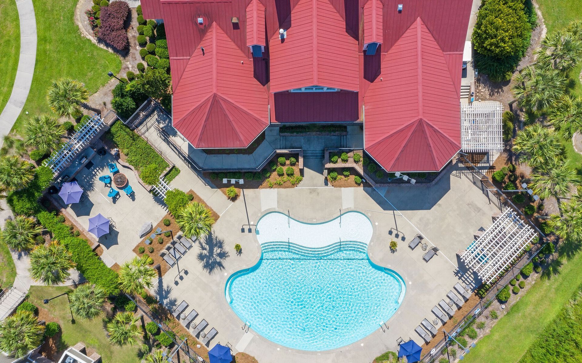 Aerial view of a red-roofed house with a backyard pool, patio seating, and landscaped garden at Grand Oaks at Ogeechee River in Savannah, GA.