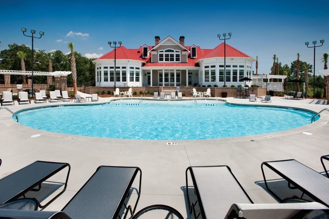 Luxury resort pool with turquoise water, lounge chairs, and a white building with a red roof in the background at Grand Oaks at Ogeechee River in Savannah, GA.