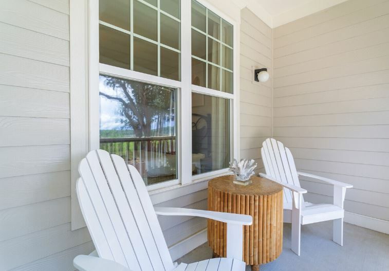 White porch with two Adirondack chairs, a small wicker table, and a window overlooking the water at Grand Oaks at Ogeechee River in Savannah, GA.