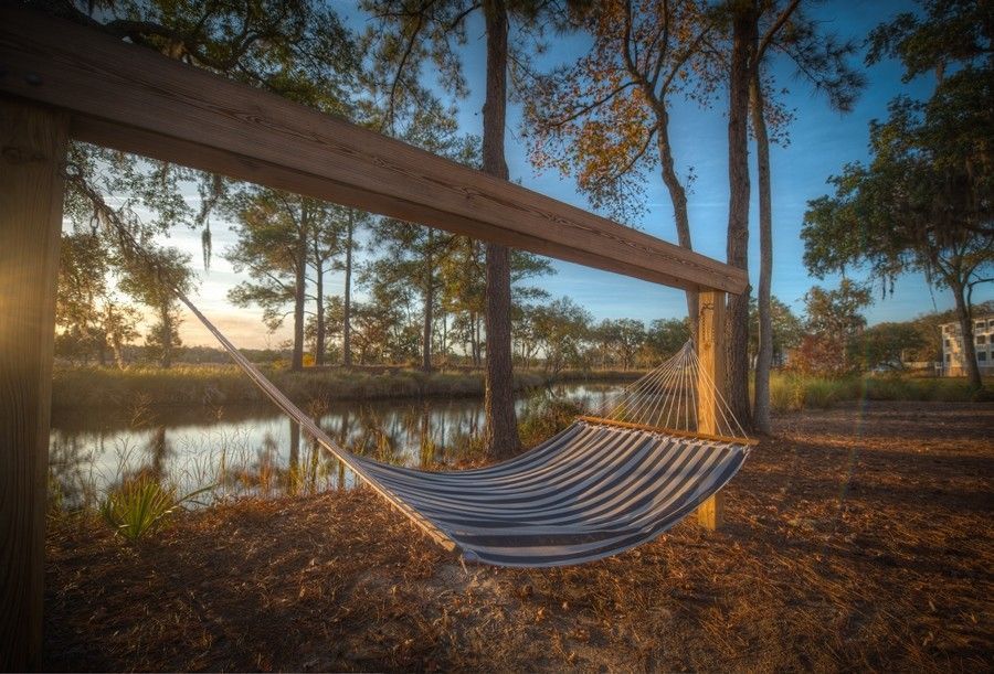 Hammock strung between wooden posts beside a calm lake at sunset in a wooded area at Grand Oaks at Ogeechee River in Savannah, GA.