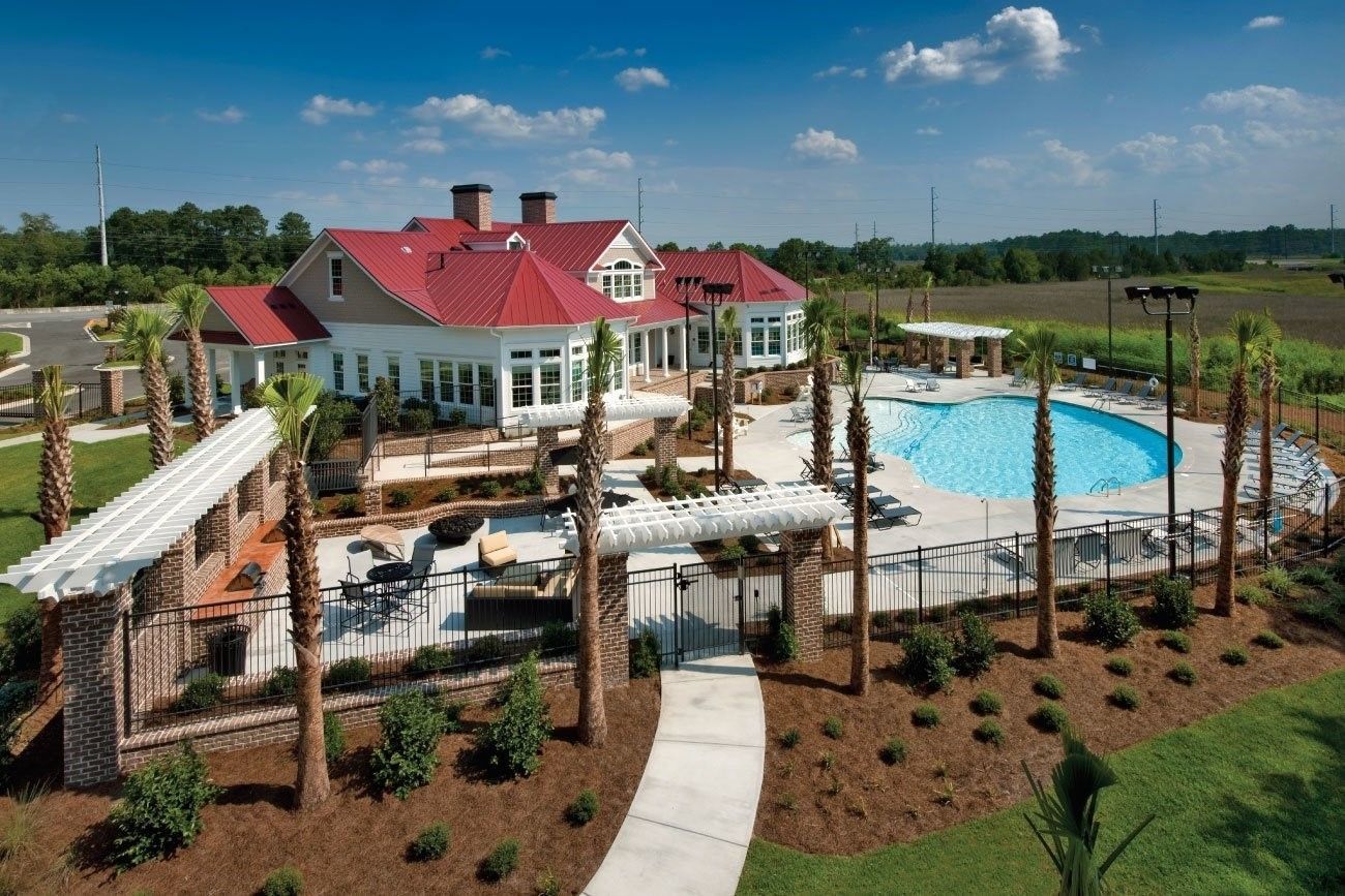 White clubhouse with red roof beside a pool and patio, surrounded by landscaping under a blue sky at Grand Oaks at Ogeechee River in Savannah, GA.