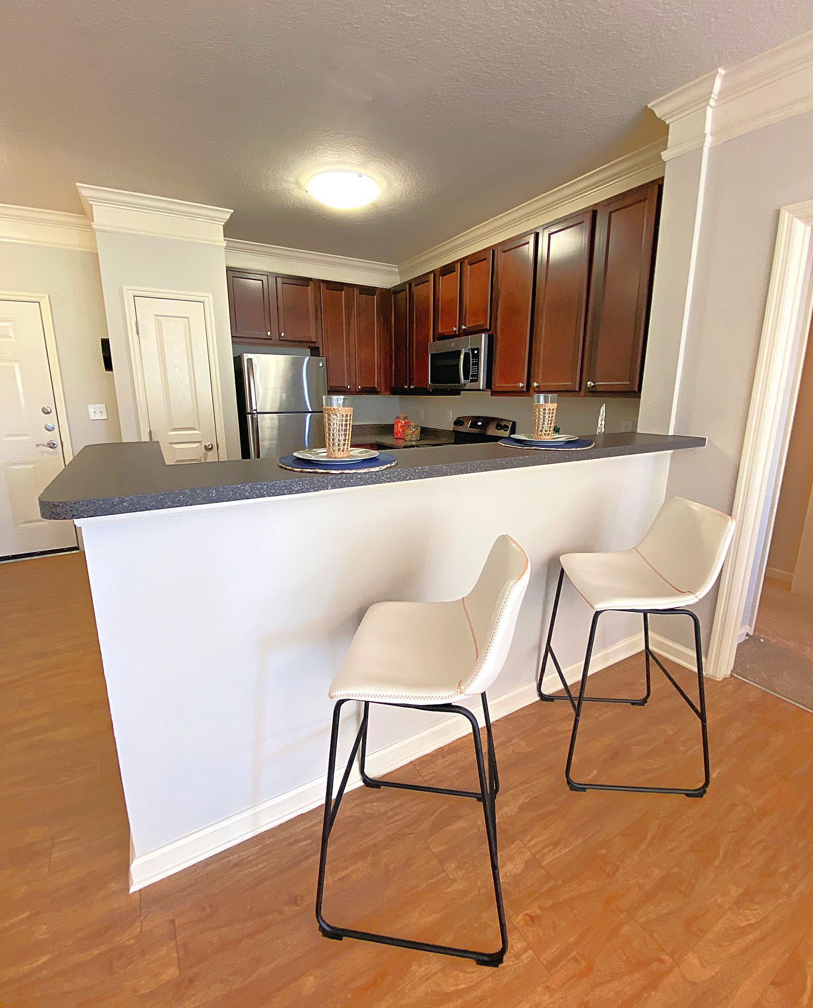 Small kitchen with white breakfast bar and two chairs, stainless fridge, and wood floors at Grand Oaks at Ogeechee River in Savannah, GA.