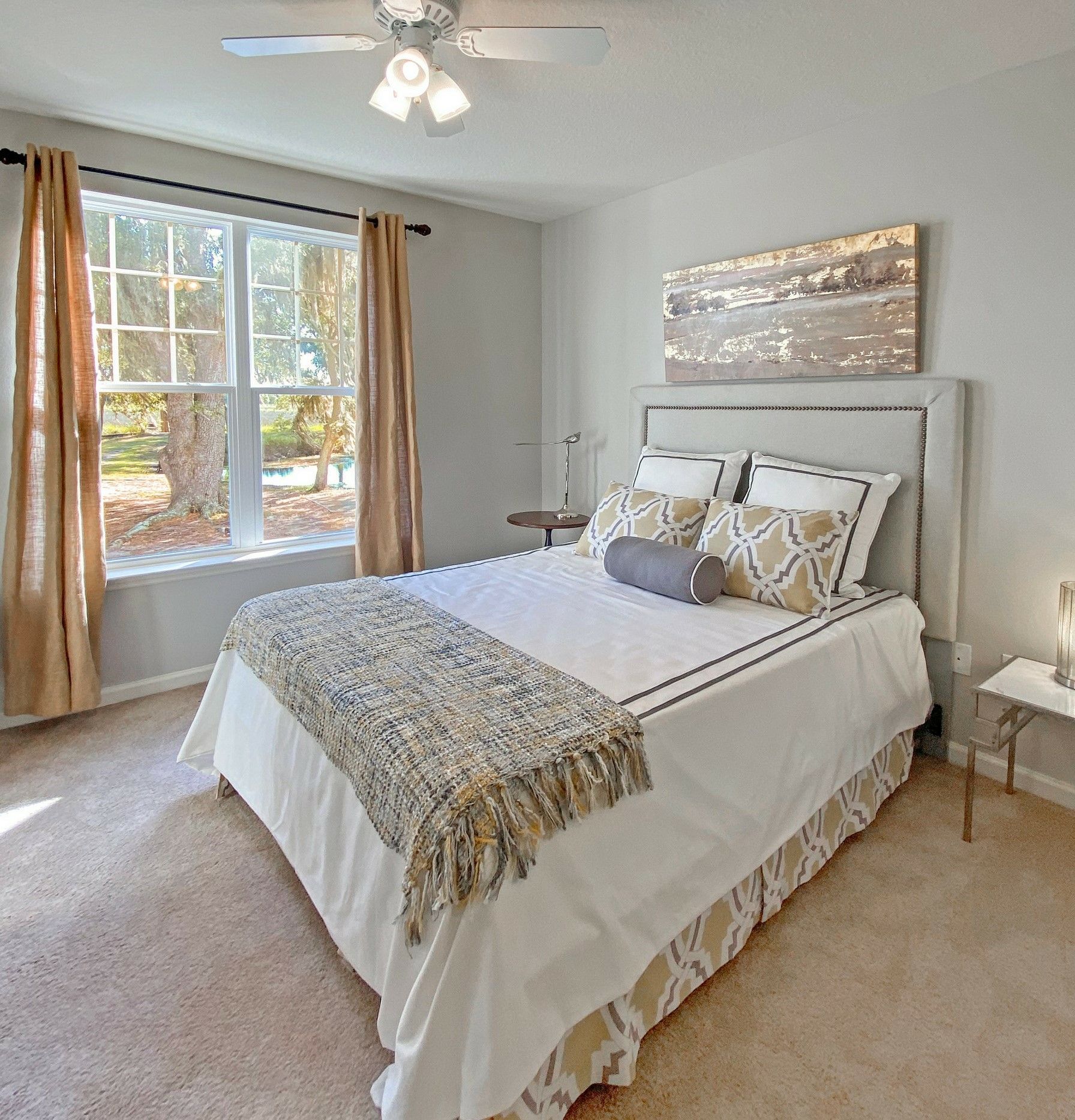 Bright bedroom with a white bed, beige carpet, window, and ceiling fan at Grand Oaks at Ogeechee River in Savannah, GA.