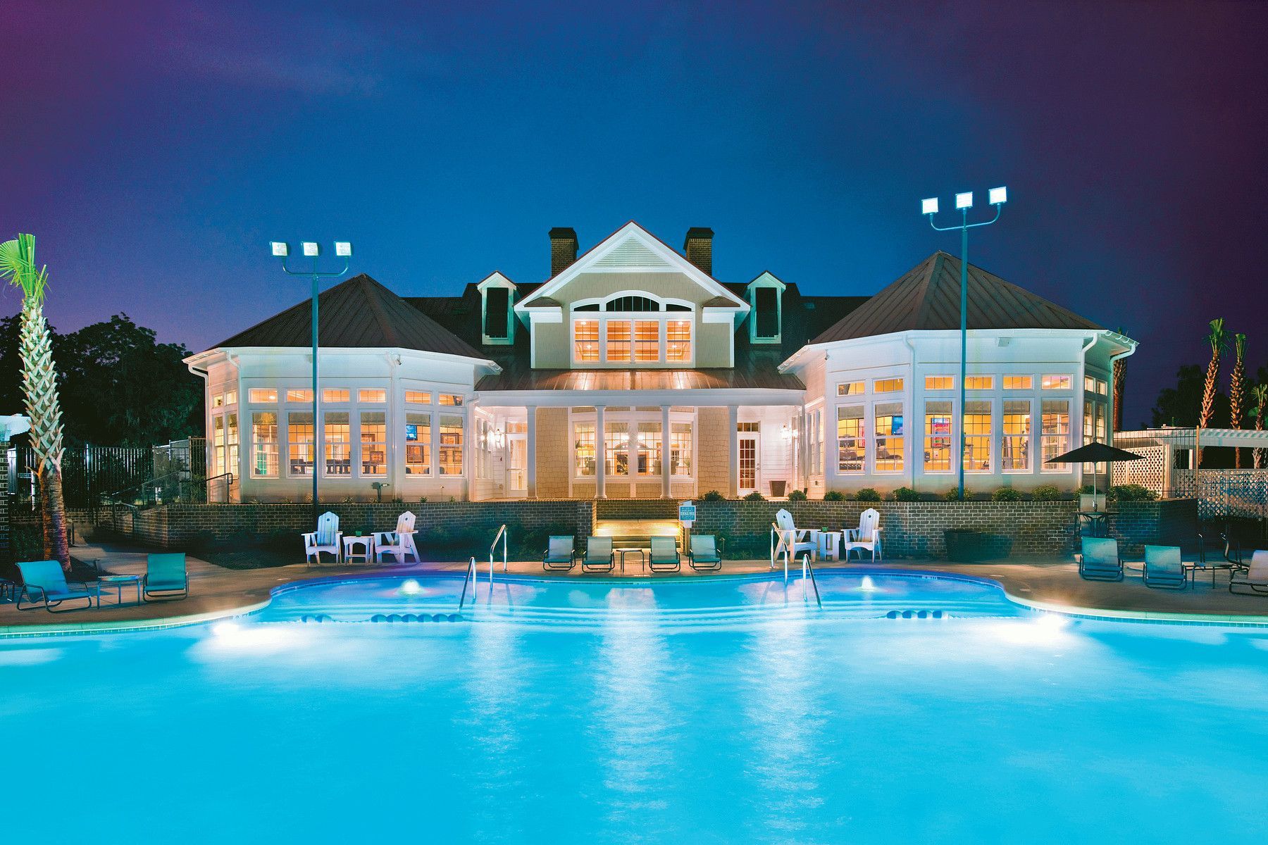 Lit resort pool at dusk with a large white building and lounge chairs reflecting in the water at Grand Oaks at Ogeechee River in Savannah, GA.