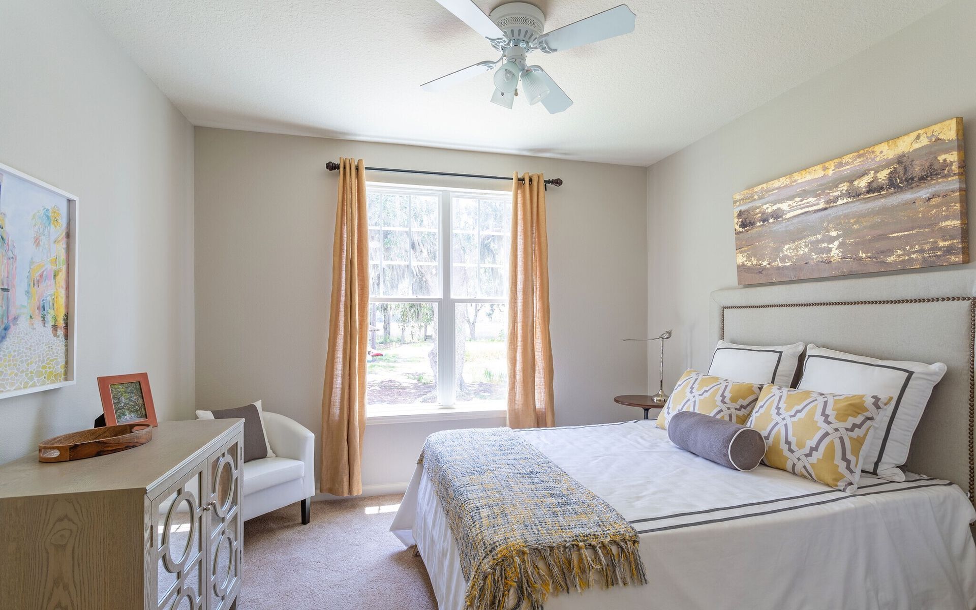 Bright bedroom with a white bed, gold curtains, desk, and ceiling fan at Grand Oaks at Ogeechee River in Savannah, GA.