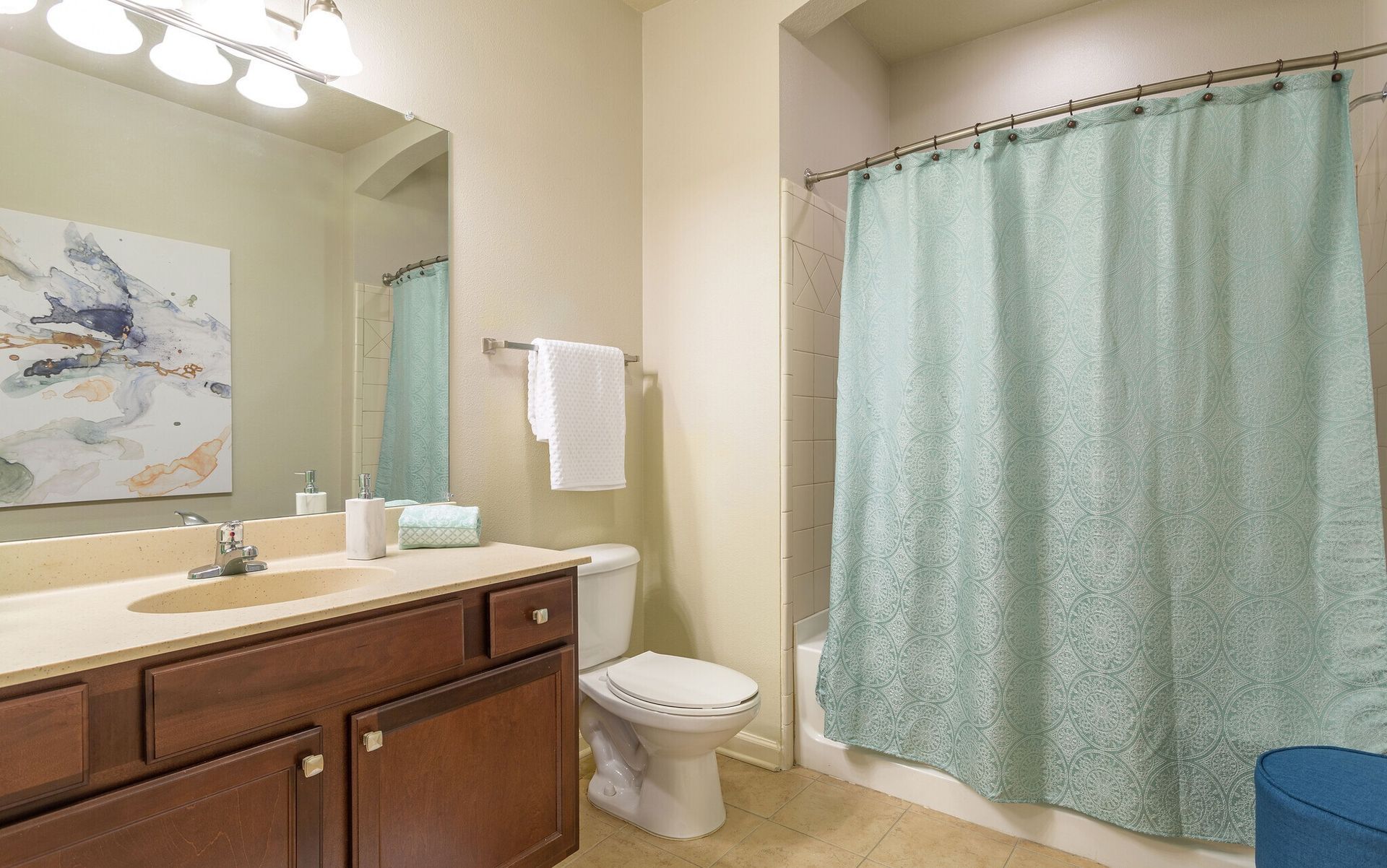 Bathroom with tan vanity, toilet, and turquoise shower curtain beside a sink and mirror at Grand Oaks at Ogeechee River in Savannah, GA.