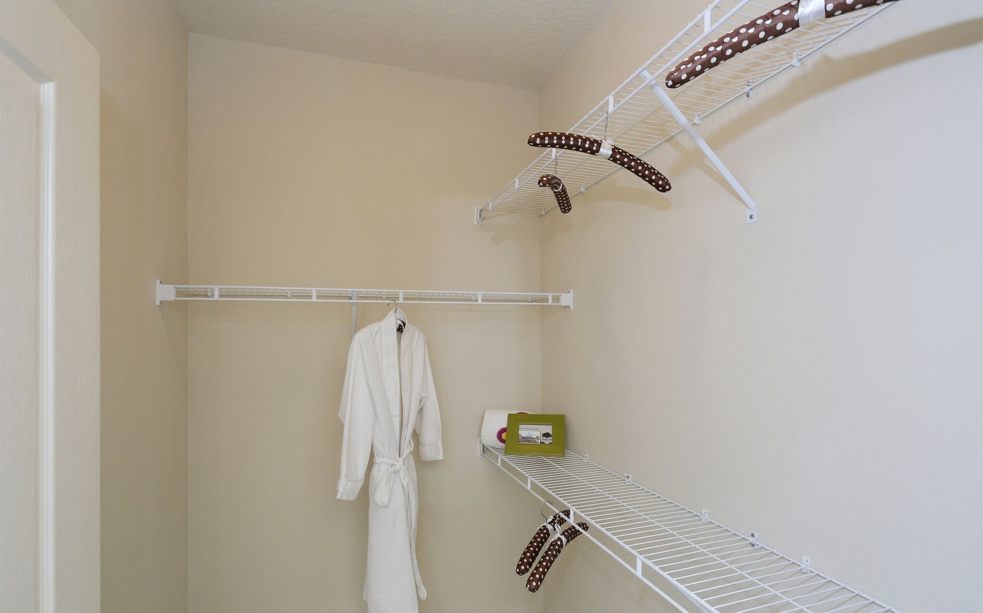 Empty walk-in closet with white wire shelves and a hanging white robe at Grand Oaks at Ogeechee River in Savannah, GA.