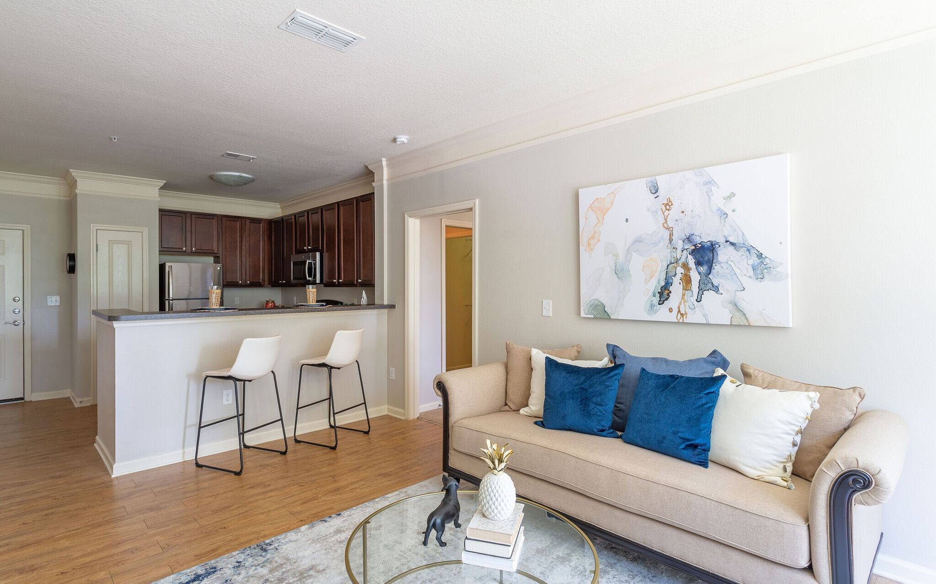 Bright living room with beige sofa, blue pillows, coffee table, and open kitchen bar stools at Grand Oaks at Ogeechee River in Savannah, GA.