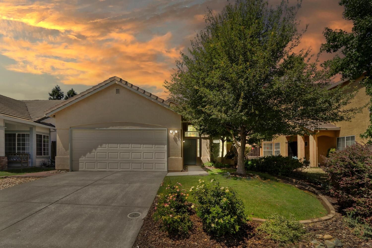 Suburban house with two-car garage, driveway, and landscaped yard at sunset