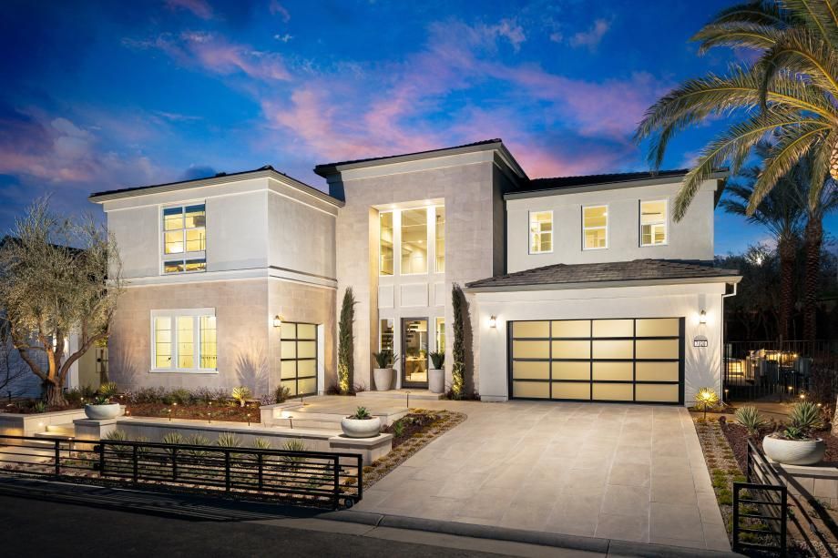 Modern two-story house at dusk with lit windows, driveway, garage, and desert landscaping