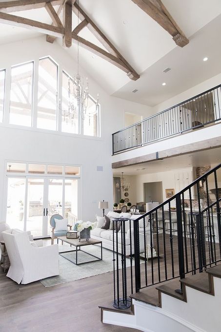 Bright modern living room with vaulted wood-beam ceiling, white furniture, and black staircase railing