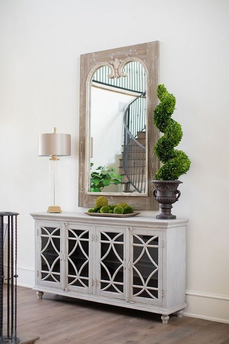 White cabinet with mirror, lamp, and topiary in a bright room