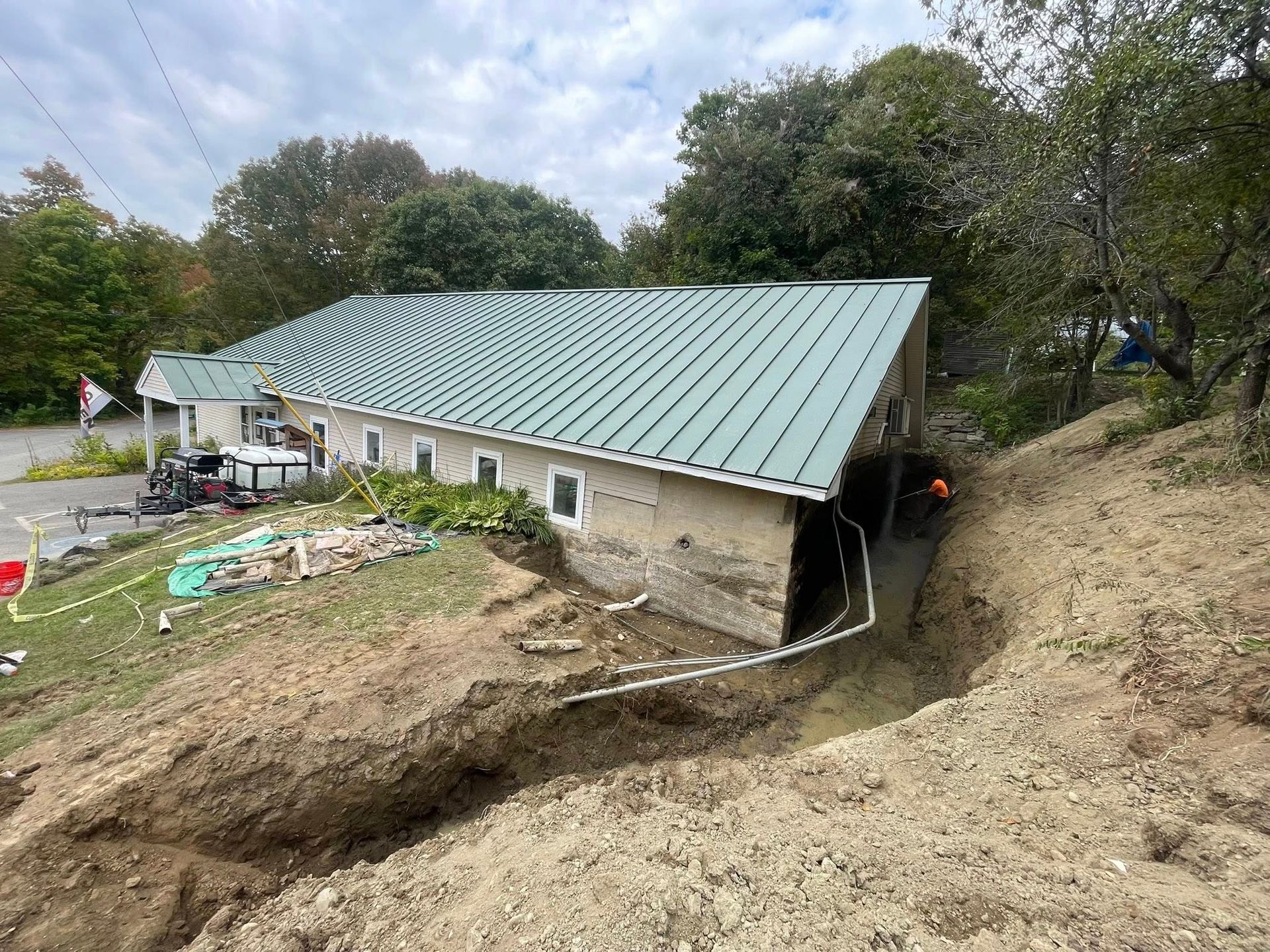 House with damaged foundation beside a deep erosion trench on a dirt hillside