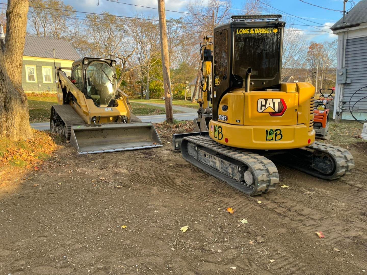 Two yellow CAT construction machines parked on a dirt lot beside a house in autumn.