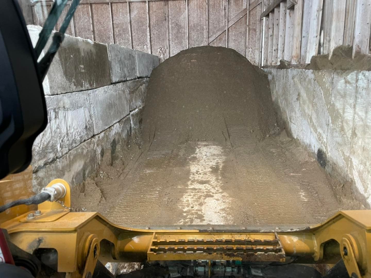Front-loader bucket dumping muddy soil into a narrow concrete bay at night