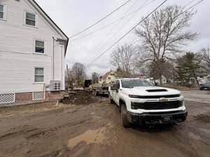 White pickup truck on a muddy residential street beside a house and construction debris