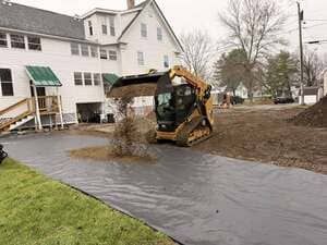 Yellow excavator beside a flooded driveway next to a white house and muddy yard