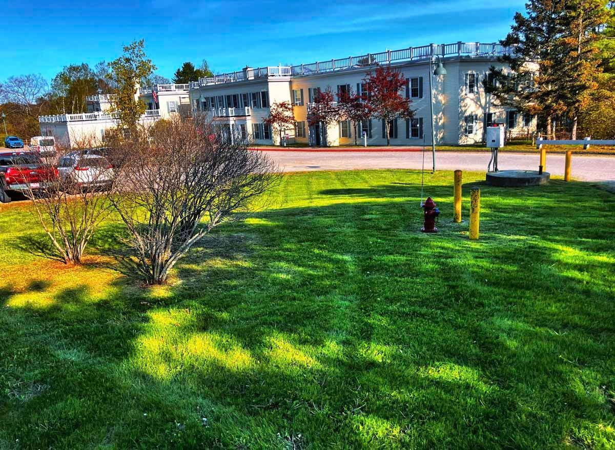 Lush green lawn in front of a white building with autumn trees and a clear blue sky