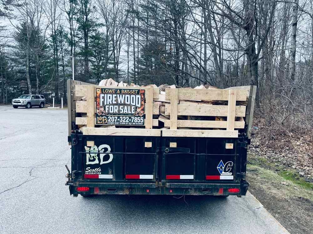 Trailer loaded with firewood for sale on a roadside, with a wooded area in the background