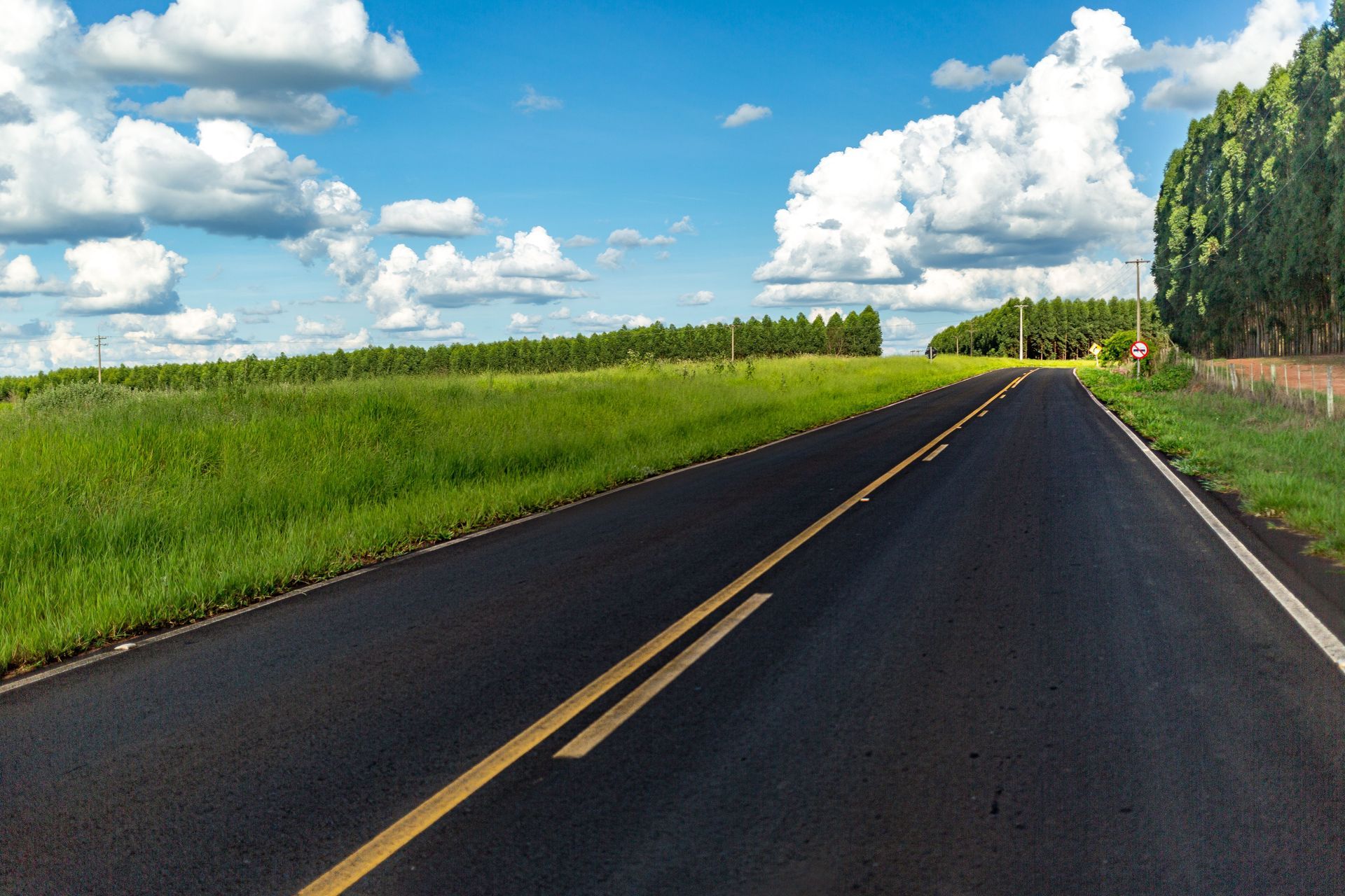 Empty rural road stretching into the distance under a blue sky with clouds