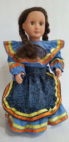 A doll wearing a blue and orange dress is standing on a white surface.
