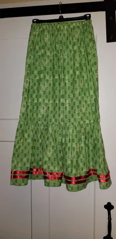 A green skirt with red trim is hanging on a hanger.