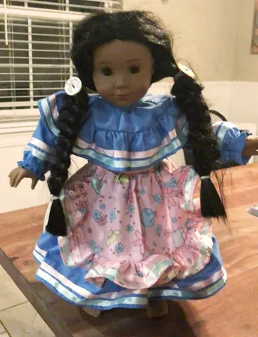 A doll is standing on a wooden table wearing a blue and pink dress