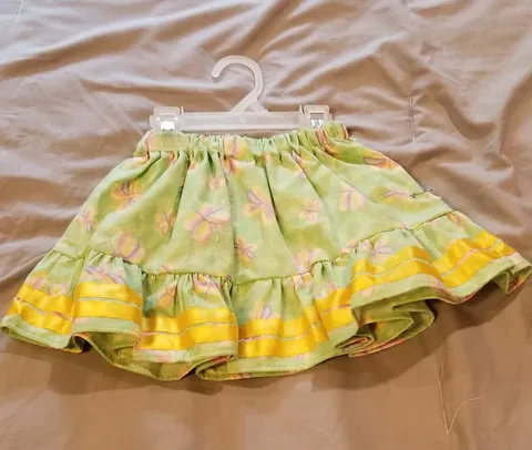 A green and yellow child skirt is hanging on a hanger on a bed.