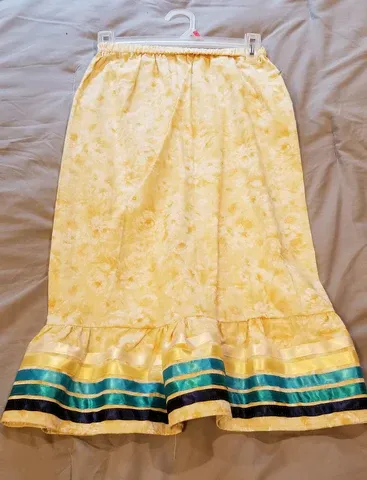 A yellow skirt with blue and black stripes is hanging on a hanger on a bed.